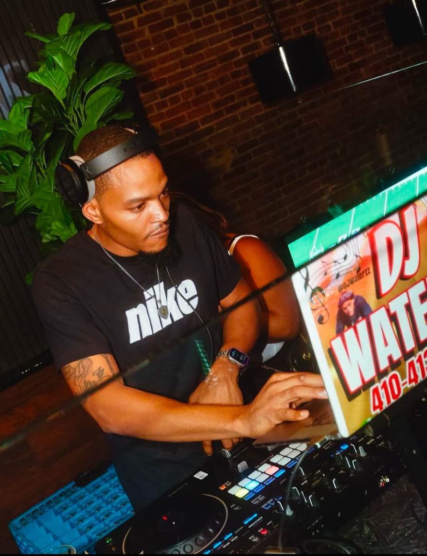 DJ wearing headphones beside a laptop and mixing controller.