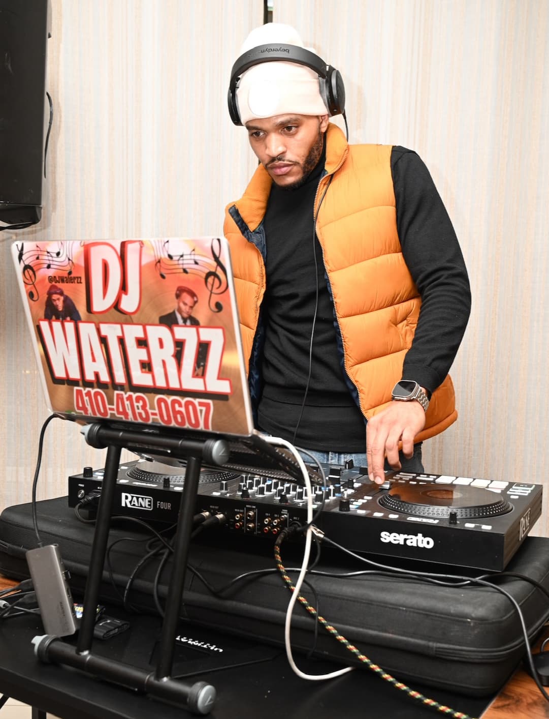 DJ wearing headphones and an orange vest at a DJ controller.