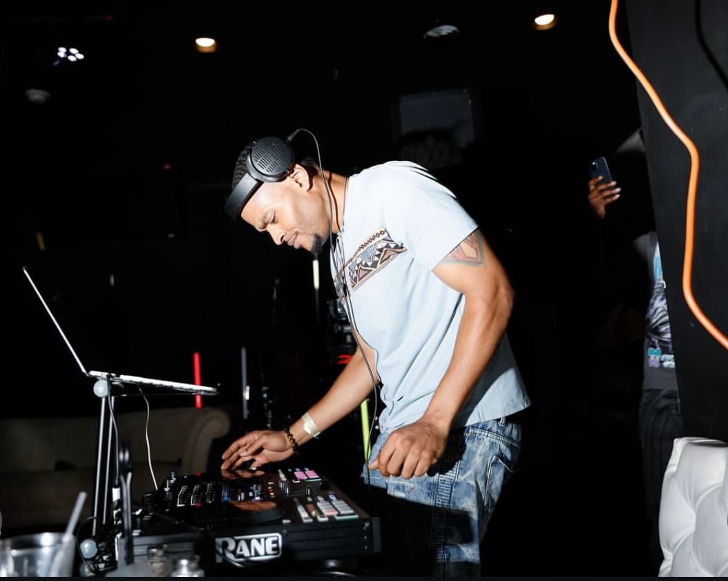 DJ in a light shirt mixing on a controller in a dark room.